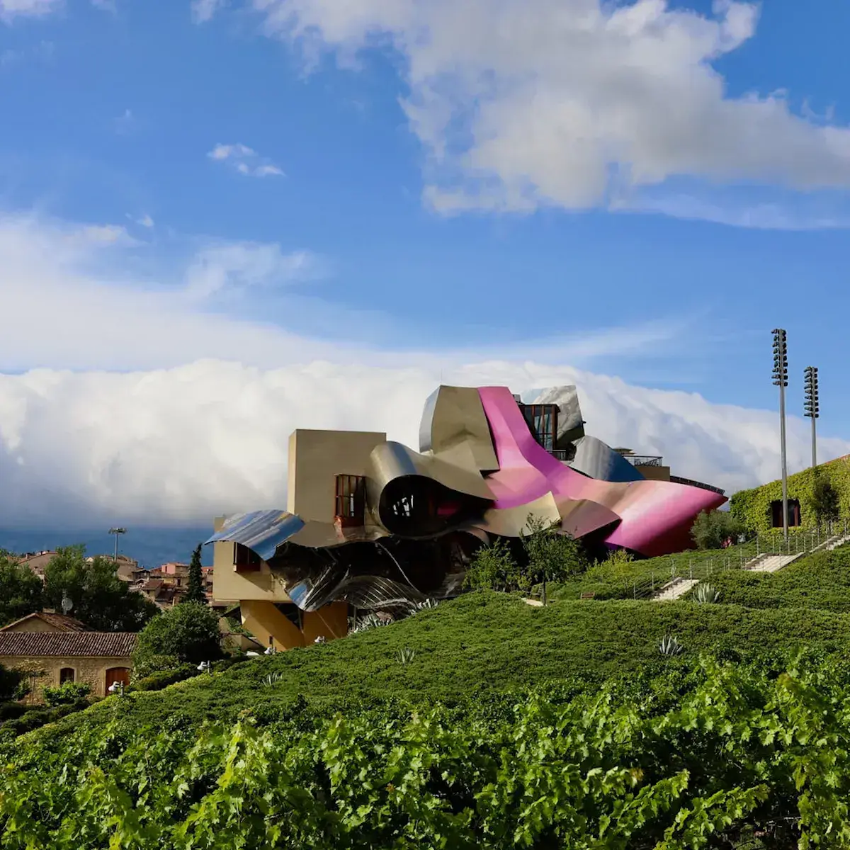Un bâtiment architectural futuriste aux formes courbes et colorées rose vif dominant des vignobles en pente verdoyante