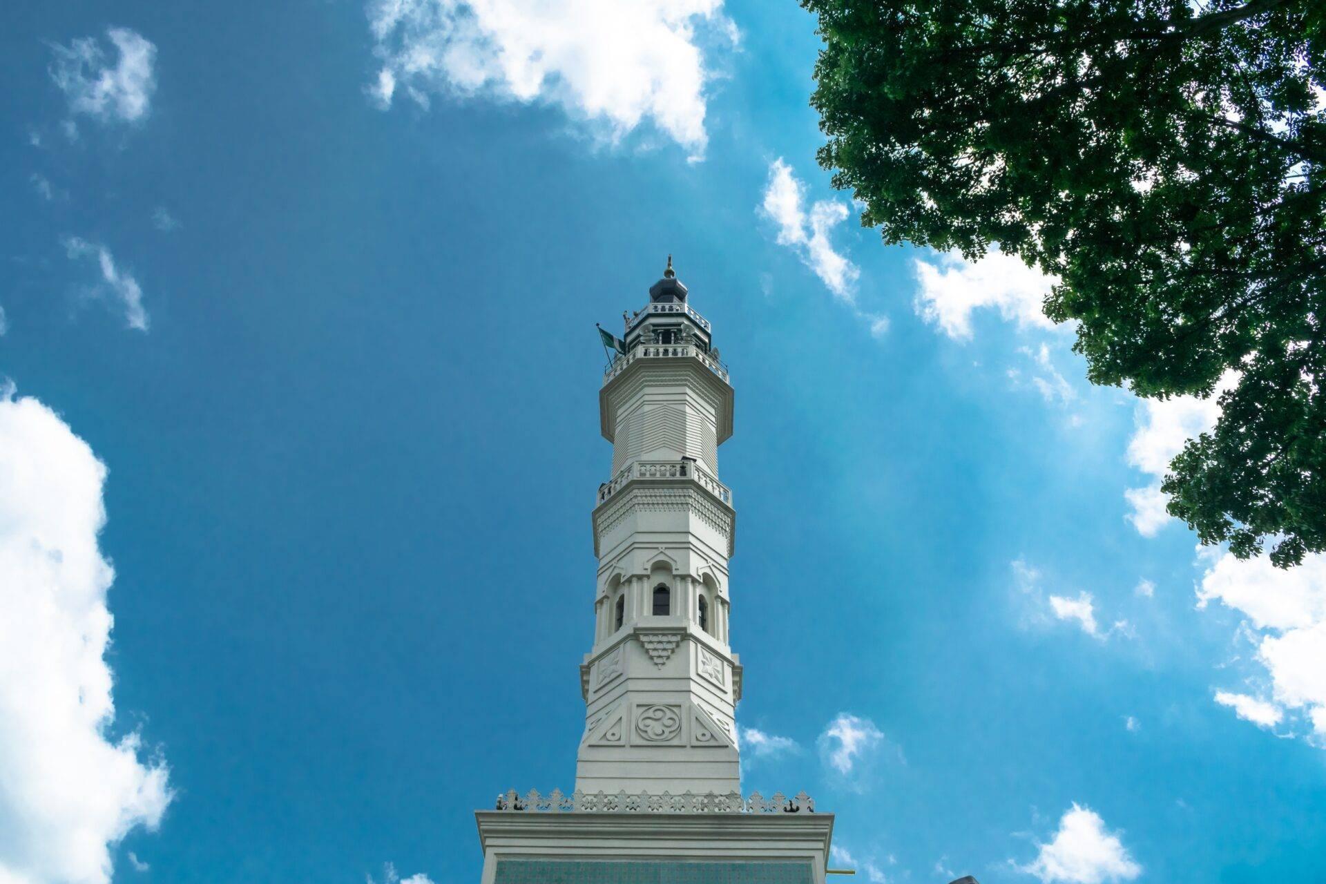 A white ornamental tower in an Asian architectural style, photographed from below against a clear blue sky