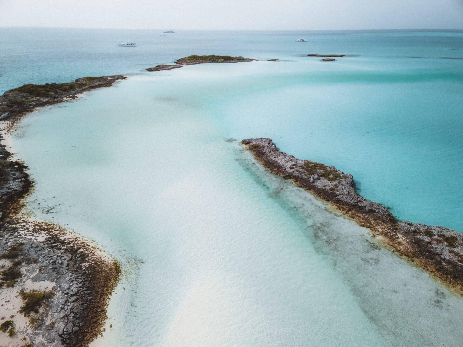 Vue aérienne d’une lagune turquoise aux Bahamas avec îlots rocheux et bateaux mouillés au large