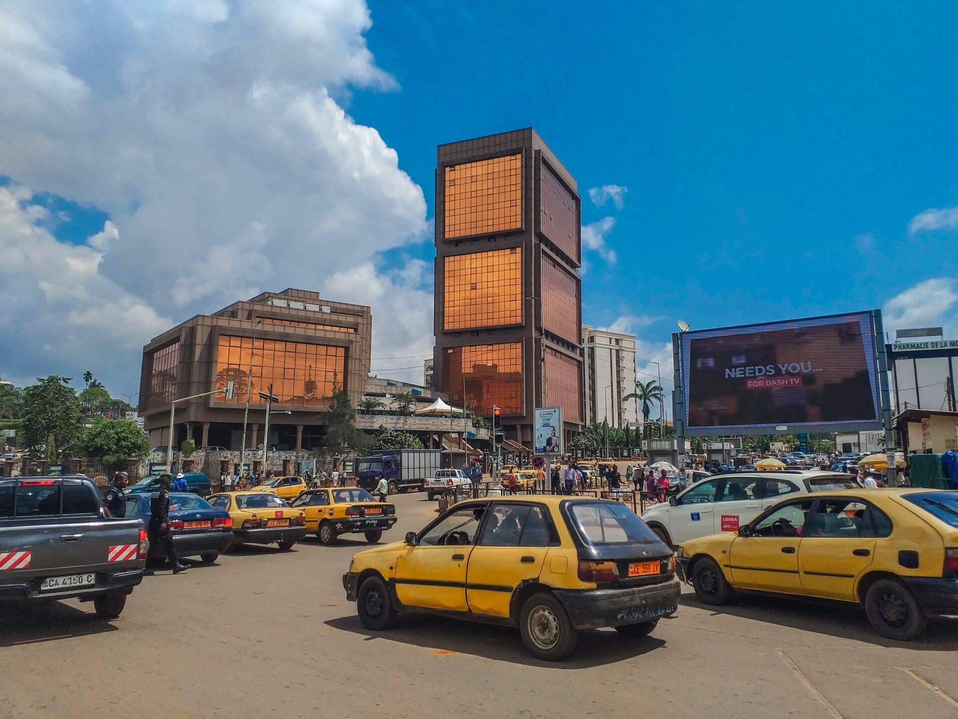 Une place urbaine animée avec des taxis jaunes et des bâtiments modernes aux façades orange sous un ciel bleu