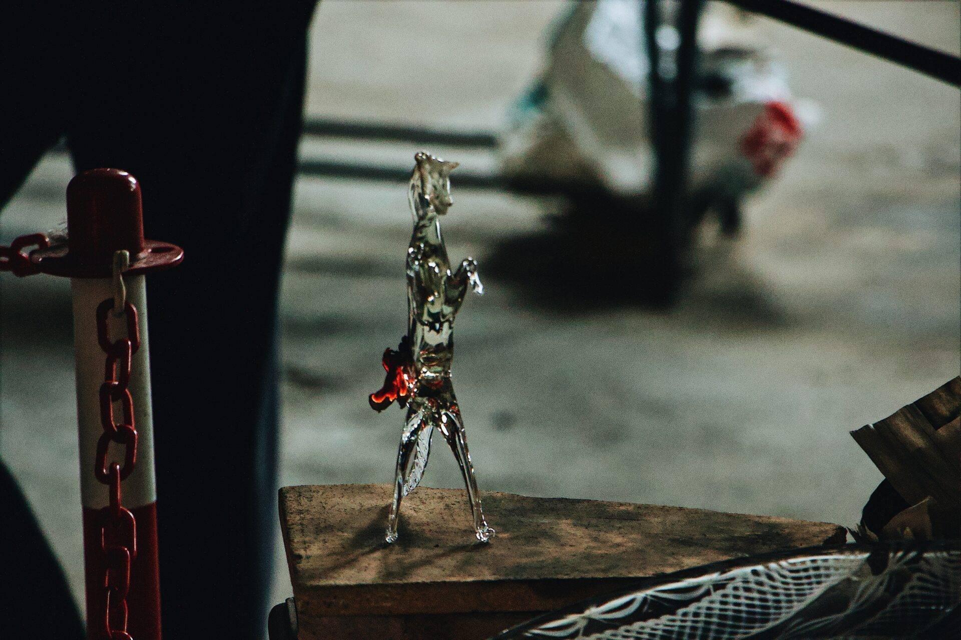 A glass figurine resting on aged wood, with a red chain and blurred objects in the background