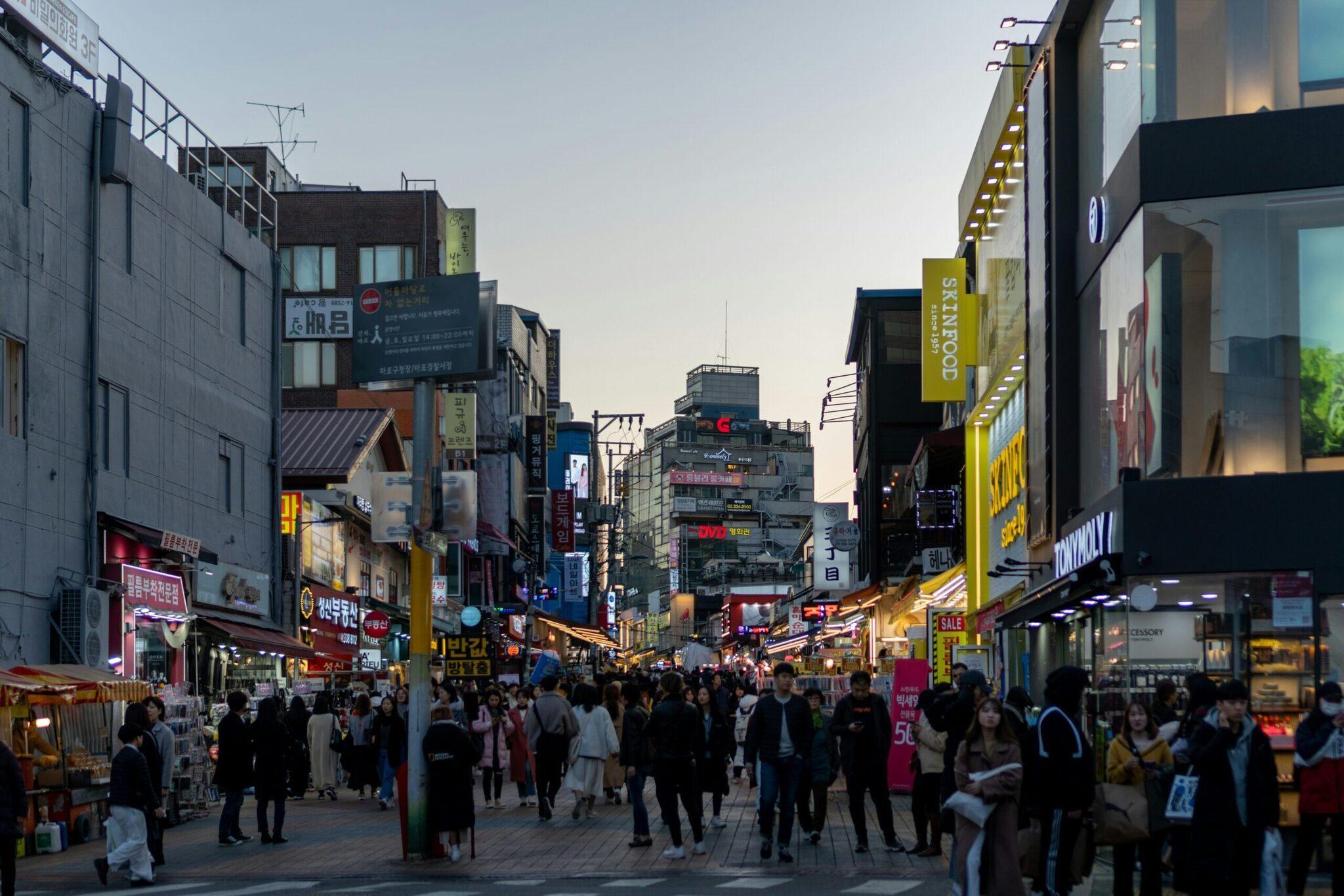 A lively Seoul shopping street with crowds, illuminated Korean signs and boutiques in the early evening