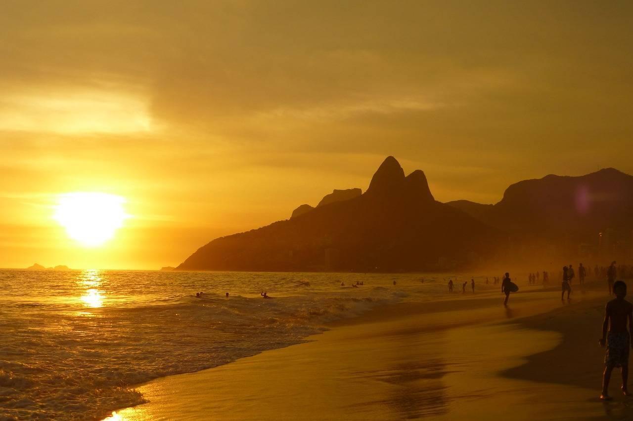 Golden sunset over a Brazilian beach with a rocky mountain silhouette and bathers on the shore
