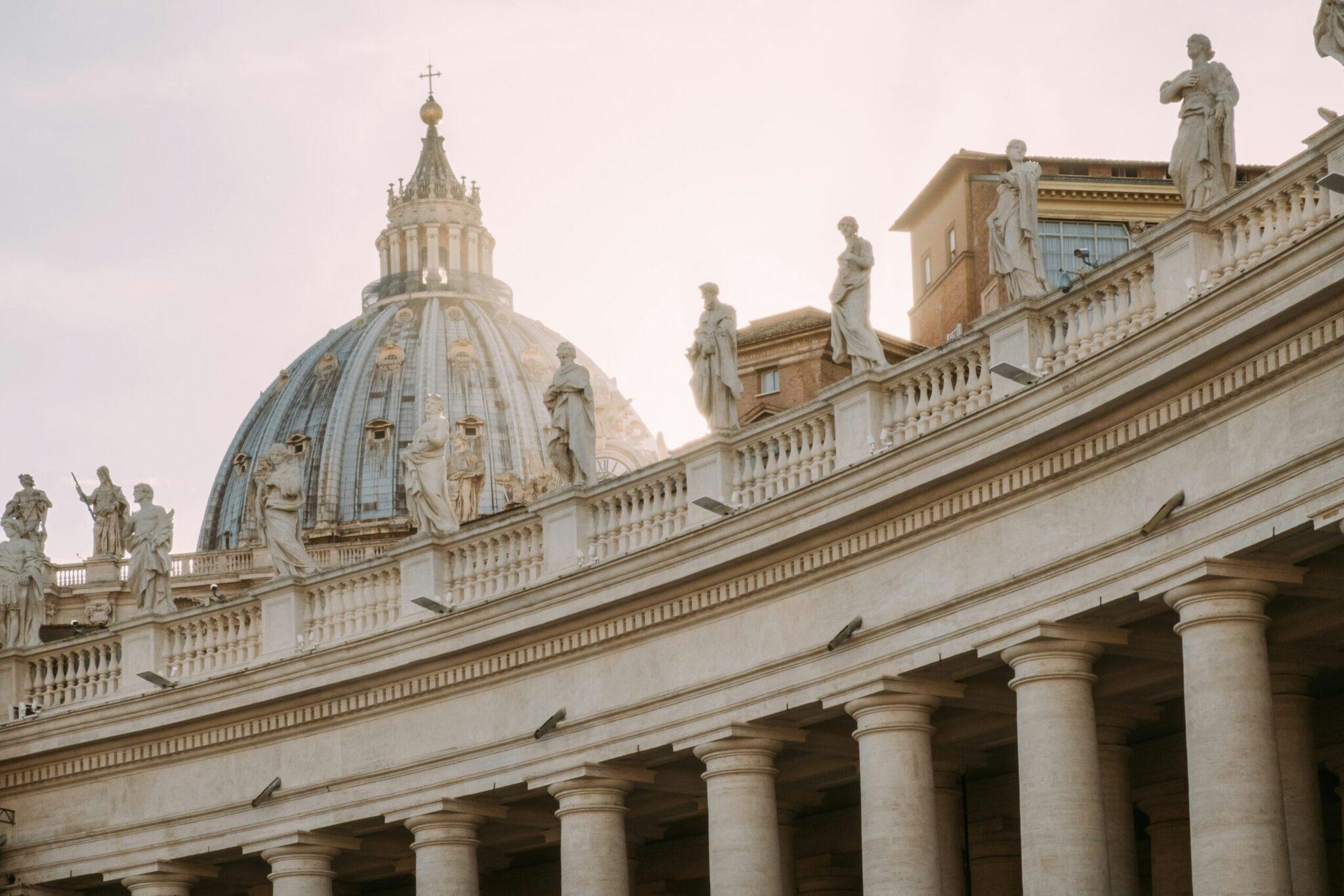Basilica colonnade and dome with statues, grand classical architecture and a clear sky