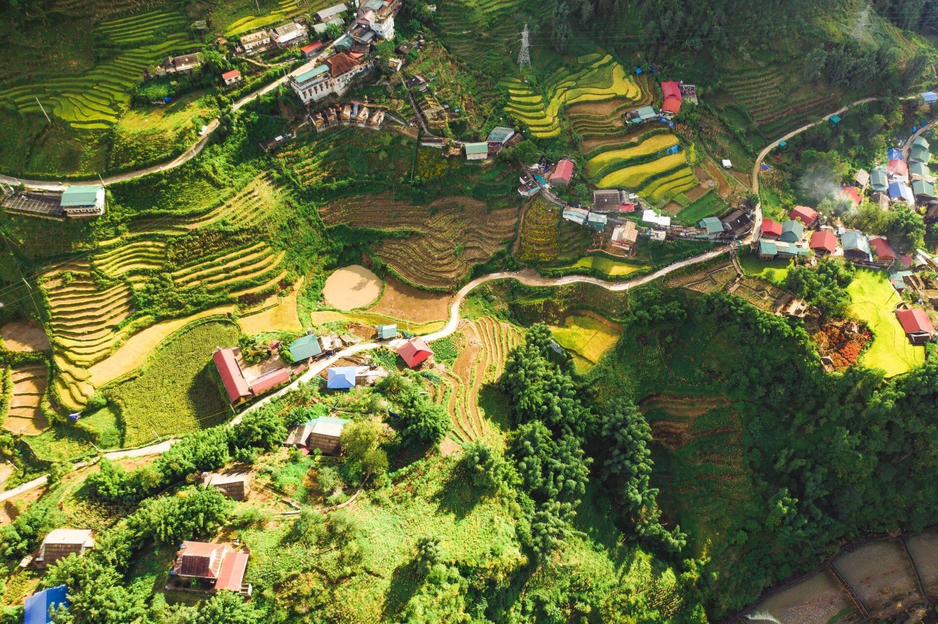 Vue aérienne de terrasses de riz en escalier avec villages éparpillés et forêts denses dans une région montagneuse d’Asie du Sud-Est