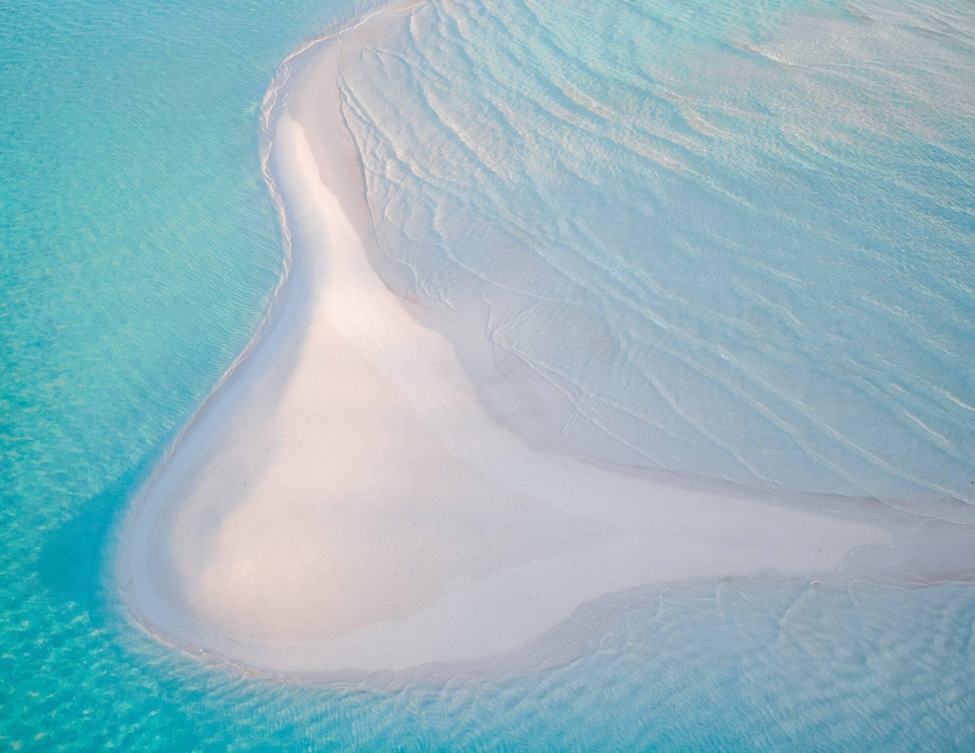 Vue aérienne d’un banc de sable blanc en forme de croissant entouré d’eaux turquoise peu profondes