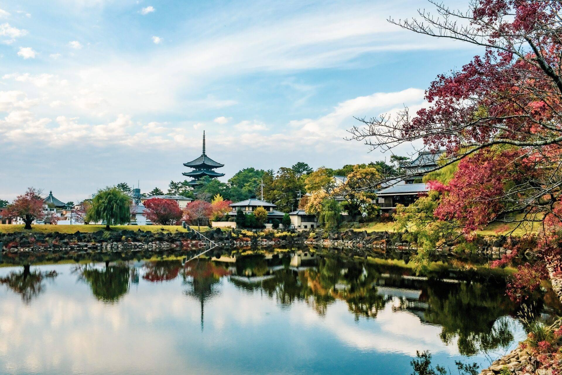 An autumnal Japanese landscape with a traditional temple reflected in a calm river, surrounded by trees in red and golden foliage