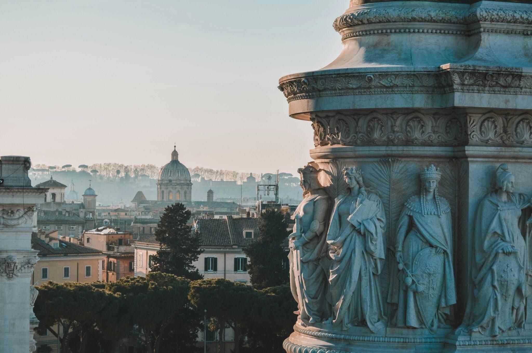 Panoramic view of Rome with classical statues in the foreground and a basilica dome visible in the urban landscape beyond
