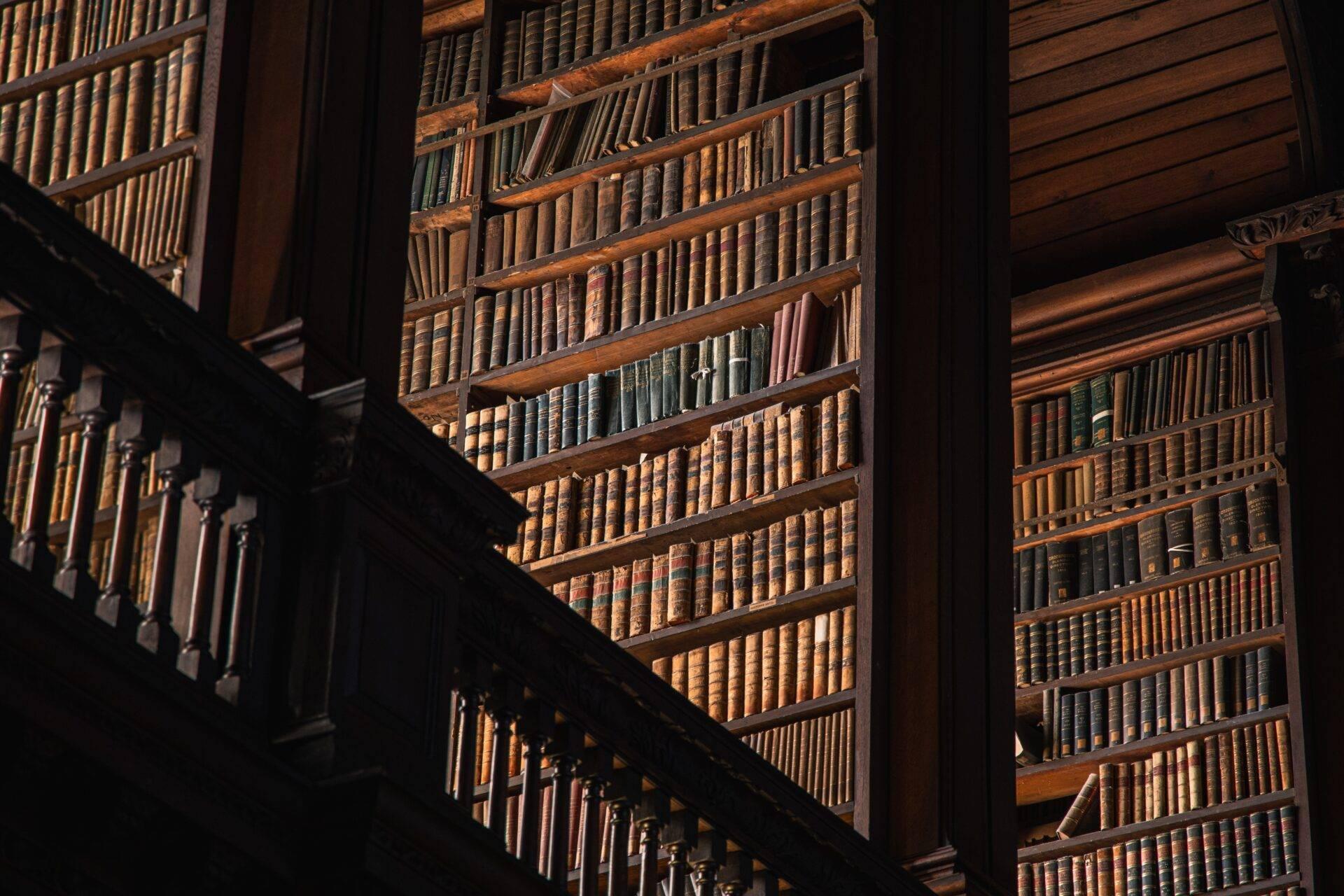 Interior of a historic library with wooden shelving filled with ancient books, a wooden staircase and natural light