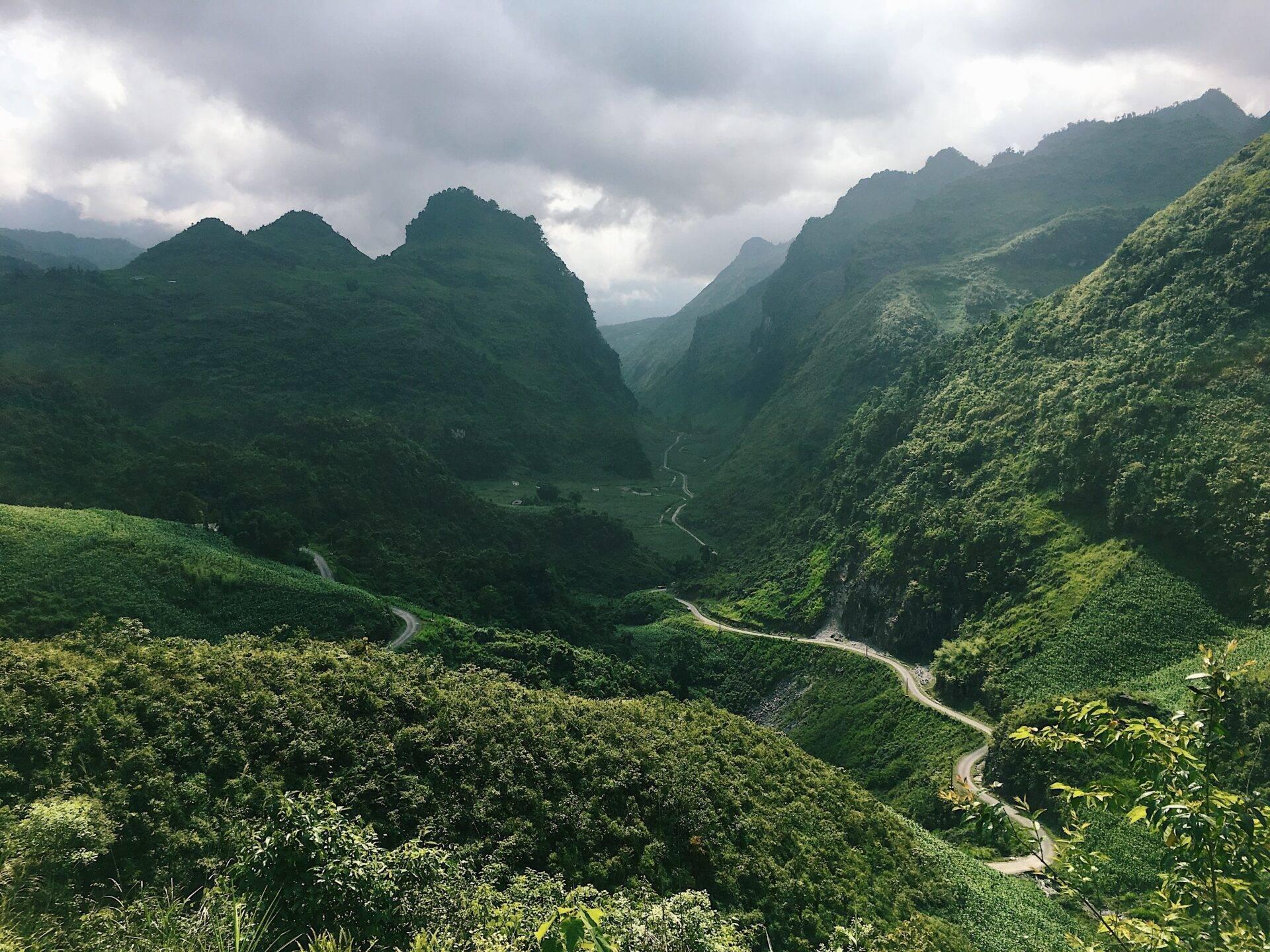Une vallée montagneuse verdoyante traversée par une route sinueuse, encadrée de pics rocheux couverts de jungle dense