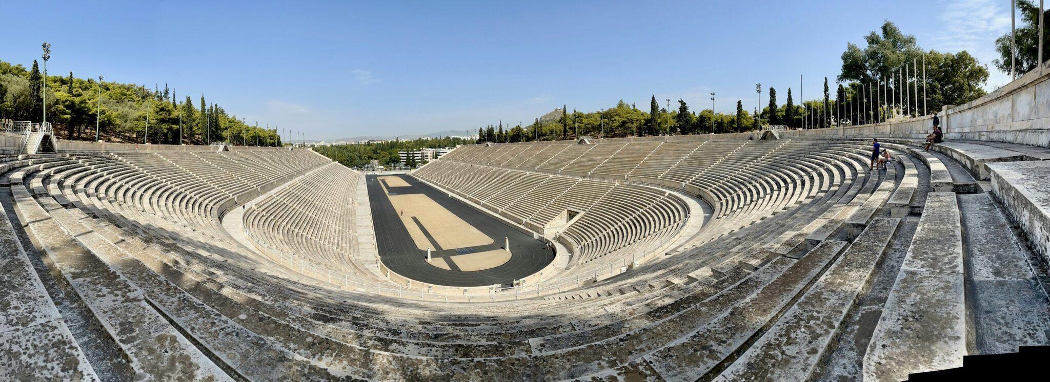 Un ancien stade amphithéâtre en marbre blanc aux gradins concentriques sous un ciel dégagé, entouré de cyprès