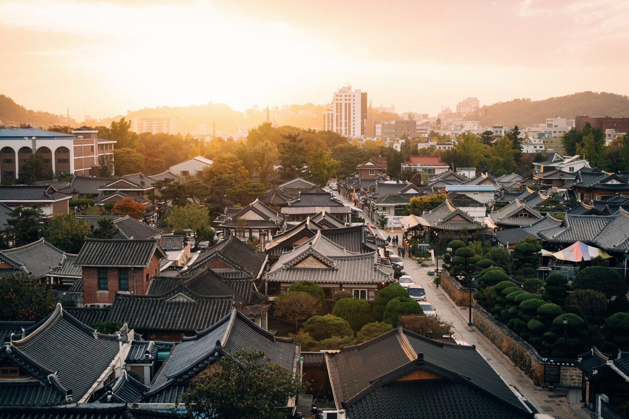 Aerial view of a traditional Korean village with curved tiled rooftops surrounded by modern skyscrapers at sunset