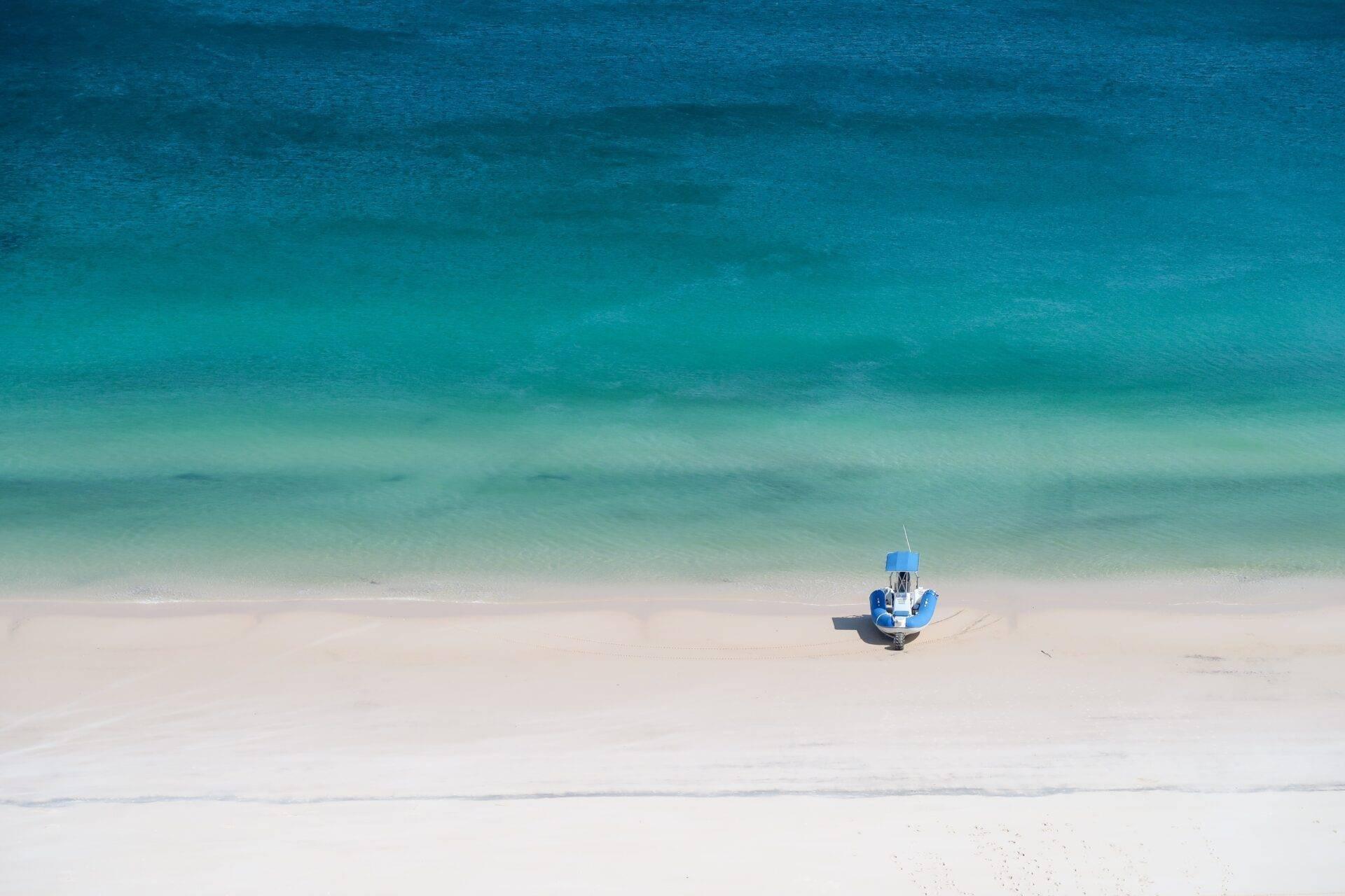 Un petit bateau de pêche bleu échoué sur une plage de sable blanc face à une mer turquoise cristalline