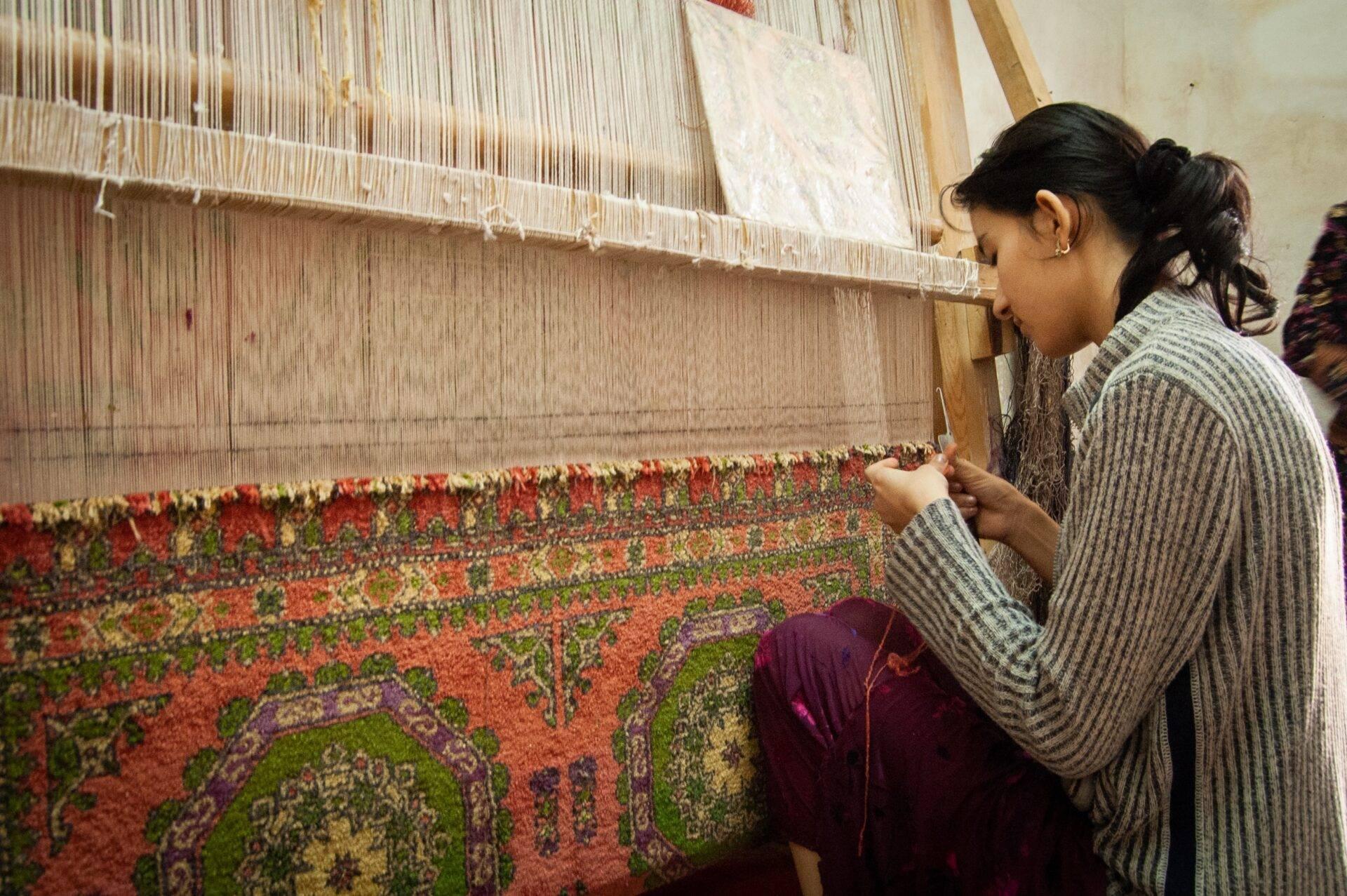 A craftswoman carefully watching the creation of a colourful traditional carpet on a hand loom