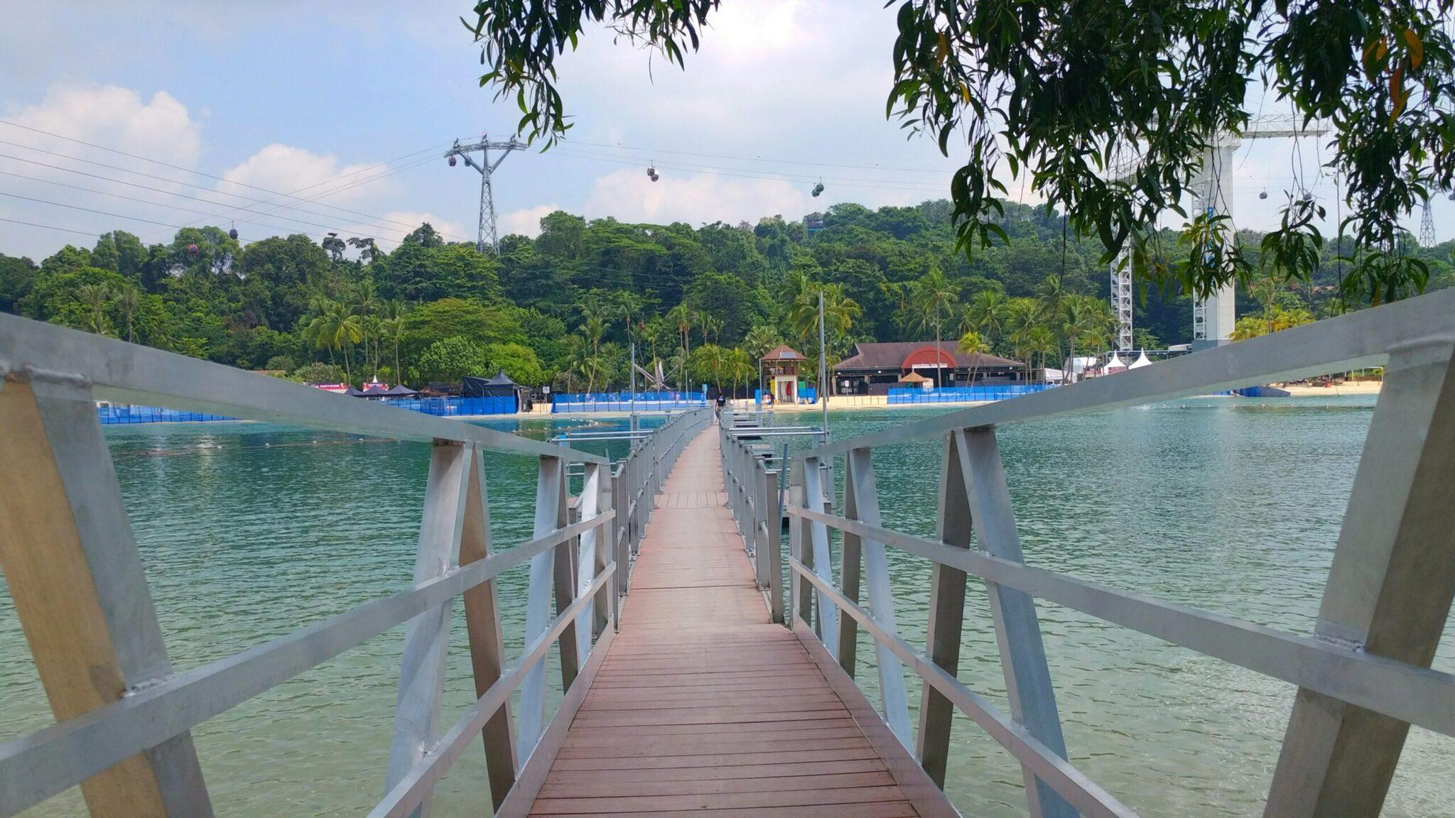 Ponton en bois menant à une plage de lagon artificiel entouré de forêt luxuriante et d’installations modernes