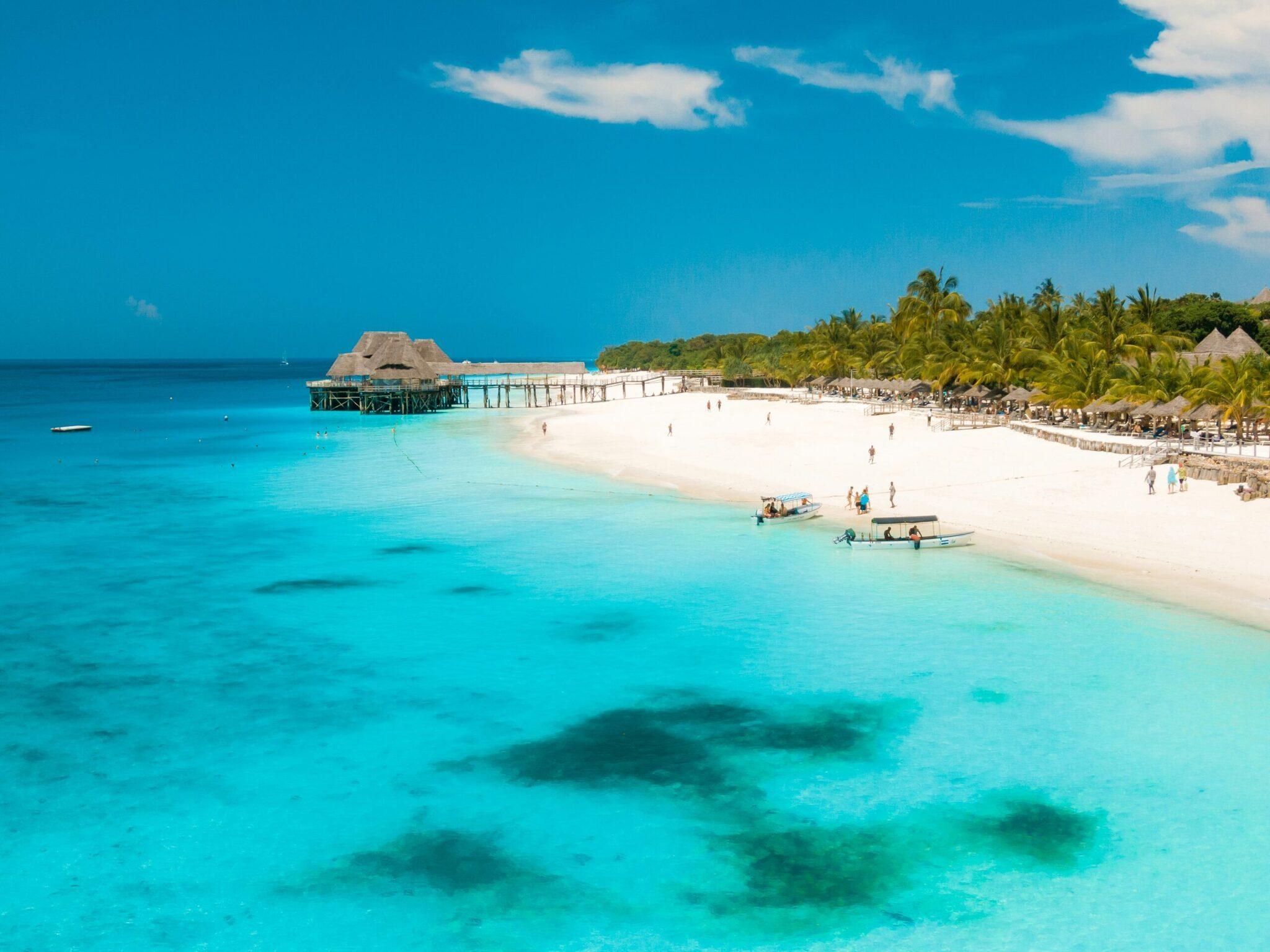 Plage tropicale aux eaux turquoise avec bungalow sur pilotis, palmiers et bateau à voile